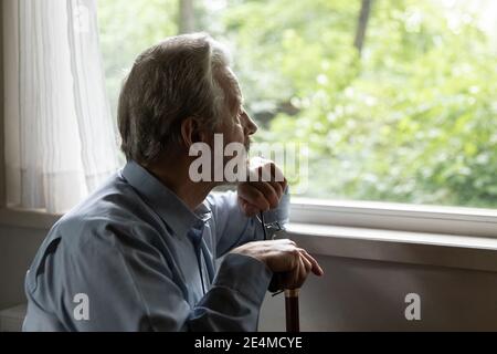 Nahaufnahme nachdenklicher reifer Mann, der Stock hält und aus dem Fenster schaut Stockfoto