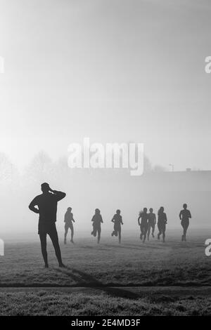 Silhouette eines Trainingscoach und einer Trainingsgruppe auf einem nebligen Feld. Stockfoto