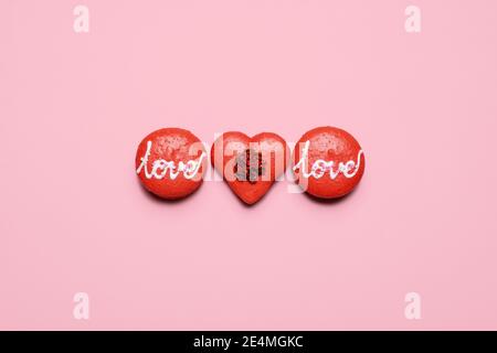 Drei Valentinstag Makronen mit Liebe in Glasur auf einem pastellrosa Hintergrund geschrieben. Drei rote und eine in Form eines Herzens mit Kopierraum und r Stockfoto