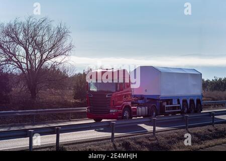 LKW mit einem speziellen Sattelauflieger für den Transport von Glas und Glas während der Fahrt auf der Autobahn. Stockfoto