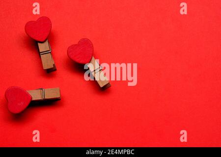 Wäscheklammer mit roter Herzform auf rotem Papierhintergrund. Valentinstag-Konzept Stockfoto