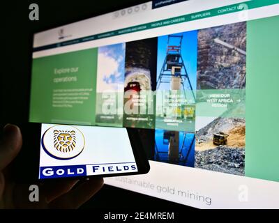 Person hält Smartphone mit Business-Logo der südafrikanischen Goldbergbau Unternehmen Gold Fields Limited auf dem Bildschirm. Konzentrieren Sie sich auf die Anzeige von Mobiltelefonen. Stockfoto
