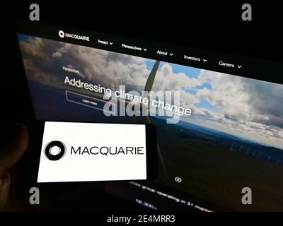 Person mit Mobiltelefon mit Logo der australischen Investmentbank Macquarie Group Limited auf dem Display vor der Website. Fokus auf Telefonbildschirm. Stockfoto