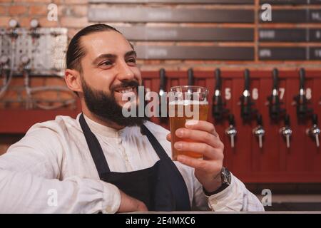 Glücklicher bärtiger Barkeeper, der in seinem Pub leckeres Bier trinkt Stockfoto
