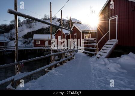 Traditionelle Rorbuer / rote Fischerhütten im kleinen Dorf Nusfjord in Lofoten, Norwegen, während eines kalten Wintersonnenaufgangs. Stockfoto