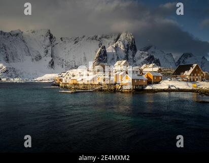 Wintersonnengang auf den traditionellen Fischerhütten in Kvalvika, in der Nähe von reine und Hamnoy, mit einer atemberaubenden Bergkulisse, Lofoten, Norwegen Stockfoto