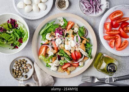 Gesunder Salat mit Tomaten, Croutons, Gemüse und Mozzarella auf einem Teller. Italienischer Panzanella-Salat mit Mini-Mozzarella-Kugeln und Kapern Stockfoto