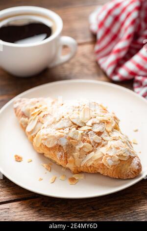 Mandelcroissant und eine Tasse Kaffee auf einem Holztisch. Frühstück im Café Stockfoto