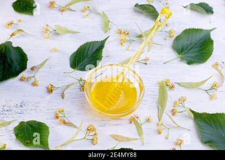 Linden Honig im Glas und Schüssel mit einem Honig Dipper auf einem weißen Holztisch. Defokusser Lindenzweig im Vordergrund. Stockfoto