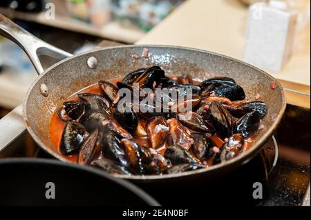 Miesmuscheln in Sahne- und Weißweinsauce werden auf dem Herd in einer Wok-Pfanne gekocht. Selektiver Fokus. Stockfoto