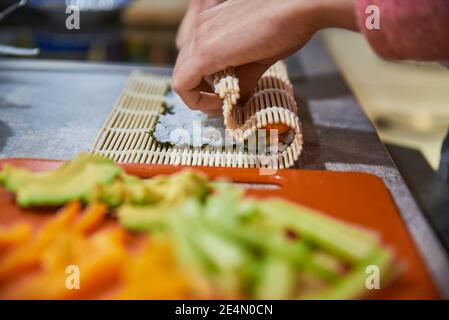 Nahaufnahme einer Person, die japanisches Essen vorbereitet. Nahaufnahme einer Person, die Sushi-Rollen zubereitet. Stockfoto