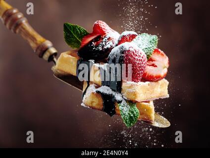 Waffeln mit Erdbeeren, Minze und Schokoladensauce, bestreut mit Puderzucker. Speicherplatz kopieren. Stockfoto