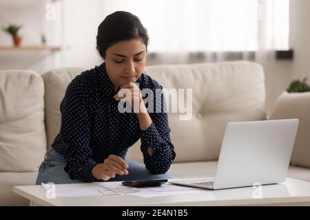 Nachdenkliche tausendjährige indische Frau sitzen auf dem Sofa berechnen Kosten Stockfoto