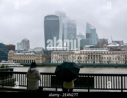 Zwei Frauen blicken über die Themse auf Schnee- und Sturmwolken, die sich in der City of London versammeln. Tief liegende Wolke verschlingt die Wolkenkratzer während es schneit Stockfoto