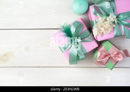 Ein zarter festlicher Hintergrund mit eingewickelten Geschenken und Kerzen auf weißem Holzhintergrund. Stockfoto