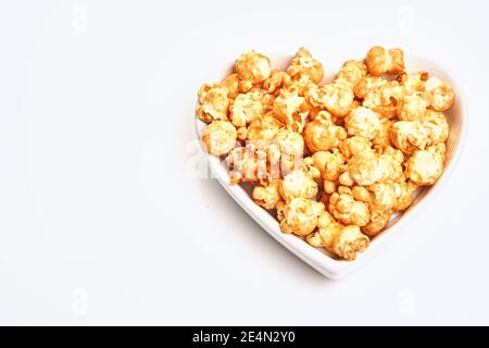 Köstliches süßes Popcorn mit Karamell in weißem Keramik-Herzteller, isoliert auf weißem Hintergrund Stockfoto