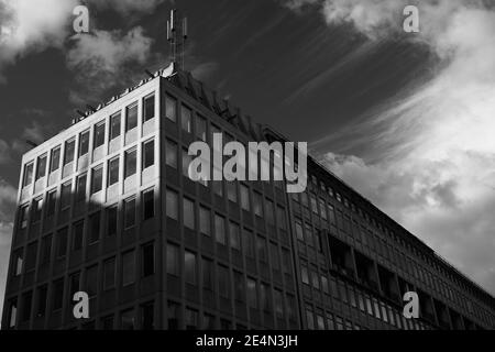 Schwarzweiß-Schwarzweißbild mit Blick auf ein Bürogebäude aus Beton aus den 1960er Jahren des 20. Jahrhunderts. Handy-Mast auf dem Dach. Sonniger Tag mit Schatten cas Stockfoto