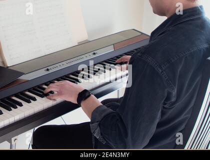 Ein junger Mann spielt den Synthesizer. Hände sind auf den Tasten. Online Klavierspielen lernen. Stockfoto