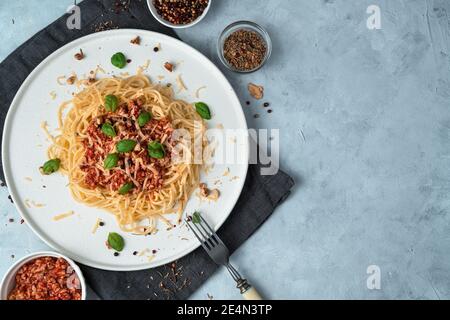 Pasta mit Sauce auf einem flachen weißen Teller auf grauem Hintergrund. Stockfoto