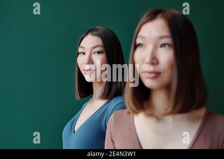 Junge Brünette weiblich von asiatischen Ethnizität mit natürlichen Make-up suchen Bei dir, während sie hinter ihrer wunderschönen Zwillingsschwester steht studio Stockfoto