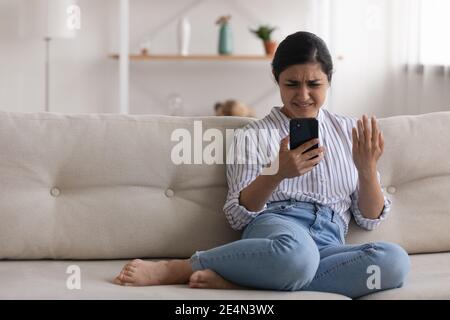 Wütend junge indische Frau lesen Spam-Nachricht auf dem Telefonbildschirm Stockfoto