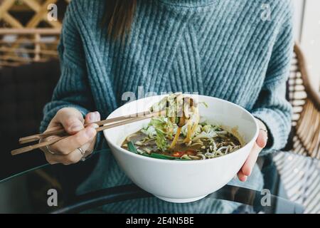 Nahaufnahme eines Mädchens, das mit Essstäbchen von Tellern der Ramen-Nudelsuppe isst. Traditionelle asiatische Küche. Stockfoto