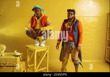 Zwei stylische Rapper im Studio, gelber Hintergrund Stockfoto
