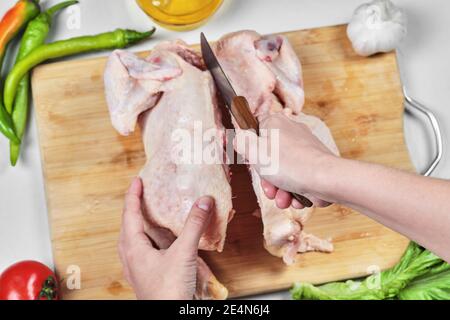 Frau Hand Schneiden roh ganze Huhn mit Messer auf Holz Schneidebrett Stockfoto