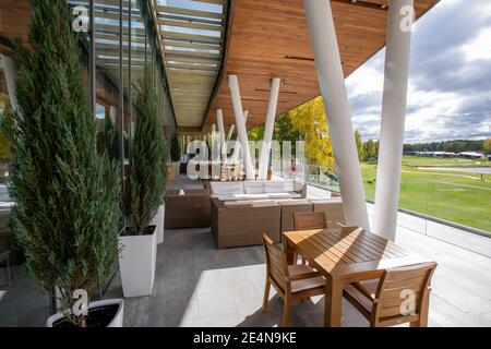 Holztisch und Stühle, Sofas und grüne Zierbäume wachsen in Töpfen im Freien entlang der großen Fenster des modernen Business Center Stockfoto