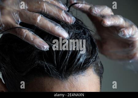 Nahaufnahme Frau Hände färben Haare. Mittlere Frau Färbung dunkle Haare mit grauen Wurzeln zu Hause Stockfoto