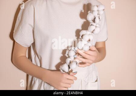 Foto von Zweig aus Baumwolle mit Kugeln in weiblichen Händen, Kleid aus natürlichen Materialien. Konzeptfoto Stockfoto