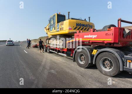 Russland, Krasnodar, Europastraße E-97: 17. September 2020-Arbeiter laden einen Komatsu Limited Raupenbagger auf ein Meusburger Transporter-Anhänger-Equipment Stockfoto