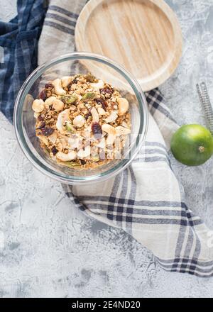 Blick von oben auf ein unbedecktes Glas voller gesunder Granola über einer rustikalen Serviette neben einer grünen Limette. Stockfoto