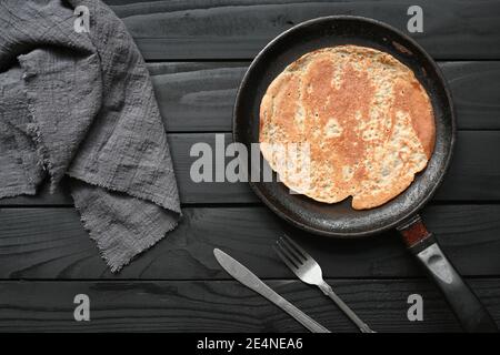 Heißer Pfannkuchen in schwarzer Pfanne auf schwarzem Tisch mit Mehl. Stockfoto