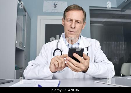 Alter männlicher Arzt hält Handy mit Handy-Telemedizin-Technologie. Stockfoto