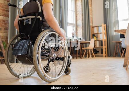 Rückansicht der jungen behinderten Frau, die im Rollstuhl sitzt Vorderseite der Kamera in der Mitte des Wohnzimmers oder Büro oder auf den Tisch zubewegen Stockfoto