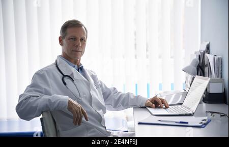 Portrait von selbstbewussten reifen Senior professionellen Arzt am Schreibtisch sitzen. Stockfoto