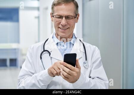 Alter männlicher Arzt hält mit Handy e Gesundheitstechnologie im Krankenhaus. Stockfoto