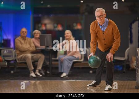 In voller Länge Porträt von aktiven Senior Mann Bowling mit Gruppe von Freunden im Hintergrund spielen, kopieren Raum Stockfoto