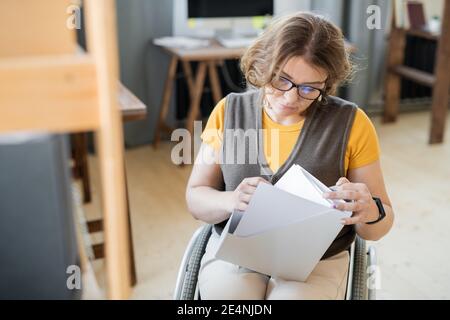 Junge attraktive Sekretärin oder Buchhalter im Rollstuhl Blick durch finanzielle Papiere in weißem Ordner, während sie im Büro sitzen Stockfoto