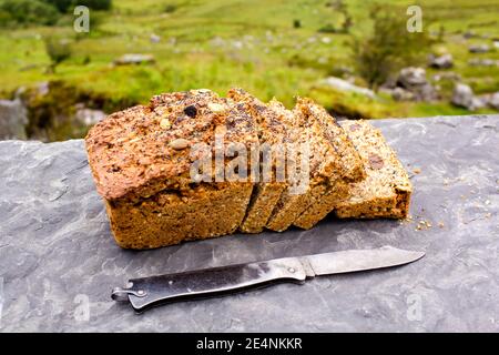 Geschnittener Laib des frischen traditionellen irischen Sodabrotes draußen mit Messer beiseite und sichtbares Grün auf dem Hintergrund. Stockfoto