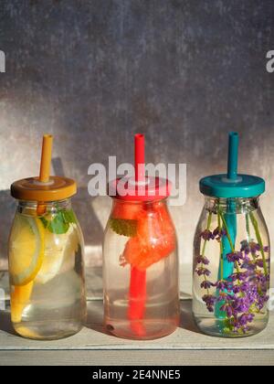 Hausgemachte Limonaden in Flaschen mit bunten Kappen und Plastikhalmen auf vintage backround. Zitrone, Melone und Lavendel. Speicherplatz kopieren. Raues Licht Stockfoto
