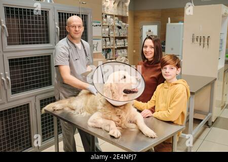 Porträt der Besitzer lächeln an der Kamera stehen in der Tierarztklinik Während der Arzt ihren Hund untersucht Stockfoto