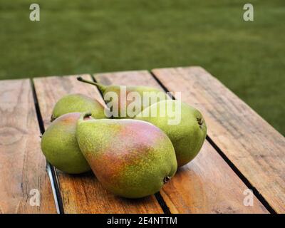 Gesunde Bio-Birnen auf Holztisch im Garten. Grünes Gras auf dem Hintergrund. Speicherplatz kopieren. Horizontale Aufnahme. Stockfoto