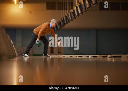 Weitwinkel Seitenansicht bei Senior Mann Bowling allein spielen, während aktive Unterhaltung in Bowlingbahn genießen, Kopierer Platz Stockfoto