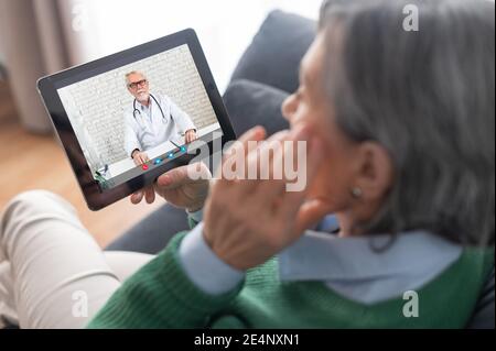 Nahaufnahme einer älteren Dame, die einen grünen Pullover trägt und eine Tablette hält und mit einem Therapeuten spricht, um sich über ihre Gesundheit zu informieren Stockfoto