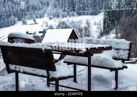 Ein Holztisch und zwei Bänke, die von Schnee bedeckt sind Die Berge Stockfoto