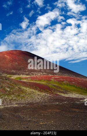 Blick über das Tal auf isolierten surrealen Kamm von kargen bunt trocken rot, schwarz und grün "bemalt" Hügel kontrastiert mit blauen Himmel, Raudaholar, Isländer Stockfoto