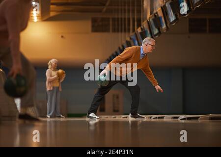 Weitwinkel Seitenansicht bei älteren Menschen Bowling spielen, während aktive Unterhaltung in Bowlingbahn genießen, Kopierer Platz Stockfoto