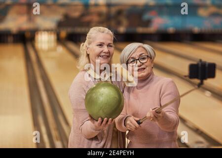 Waist-up-Porträt von zwei älteren Frauen, die Selfie-Fotos beim Bowling spielen und genießen Sie aktive Unterhaltung in Bowlingbahn, Kopierer Platz Stockfoto